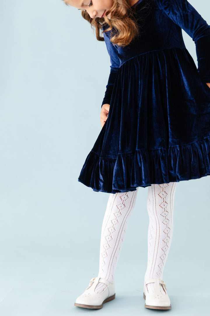 little girl in long sleeve navy blue long sleeve velvet twirl dress paired with white open knit crochet tights and white mary janes