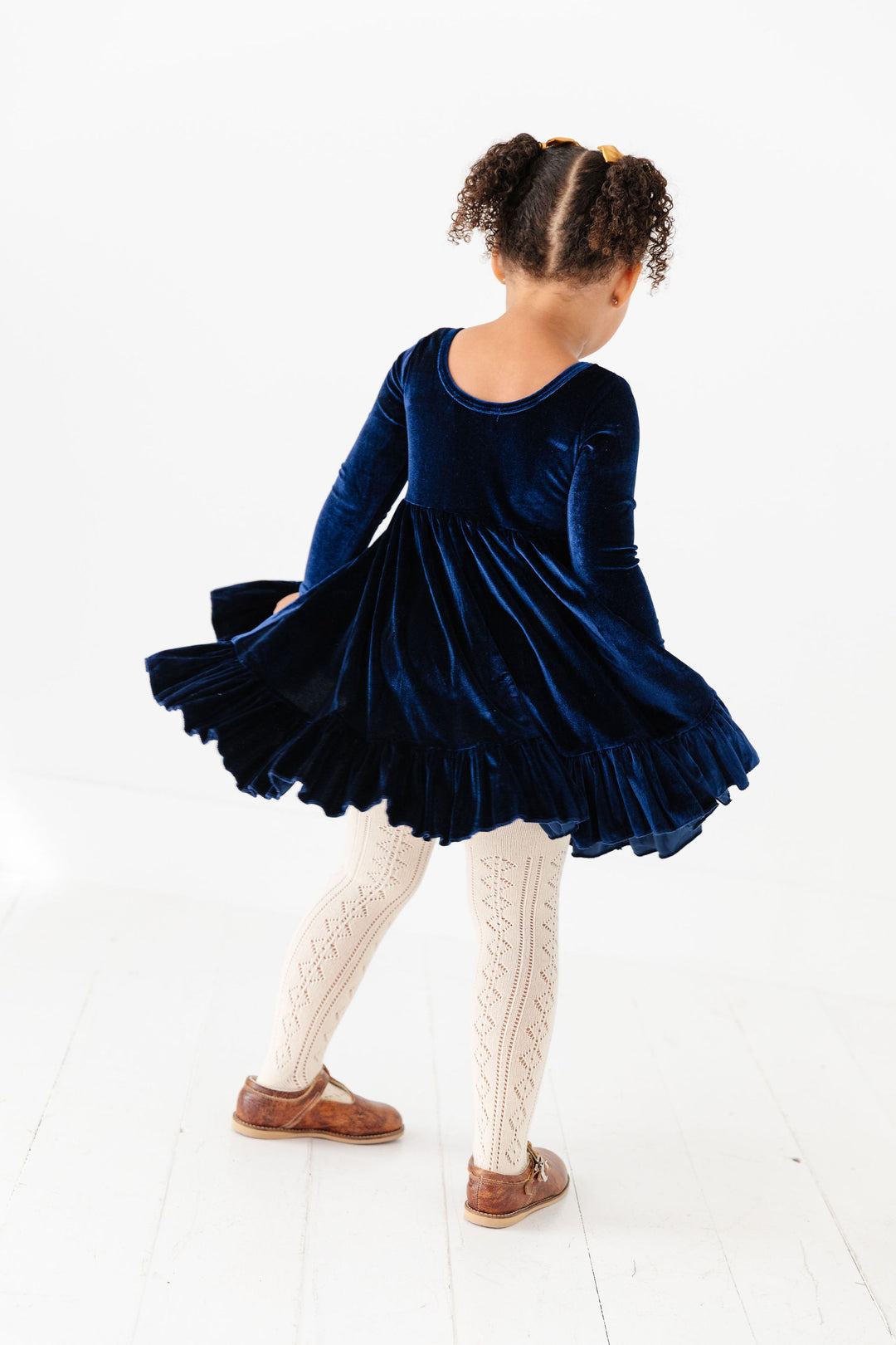 girl twirling in navy velvet dress with vanilla pointelle knit tights