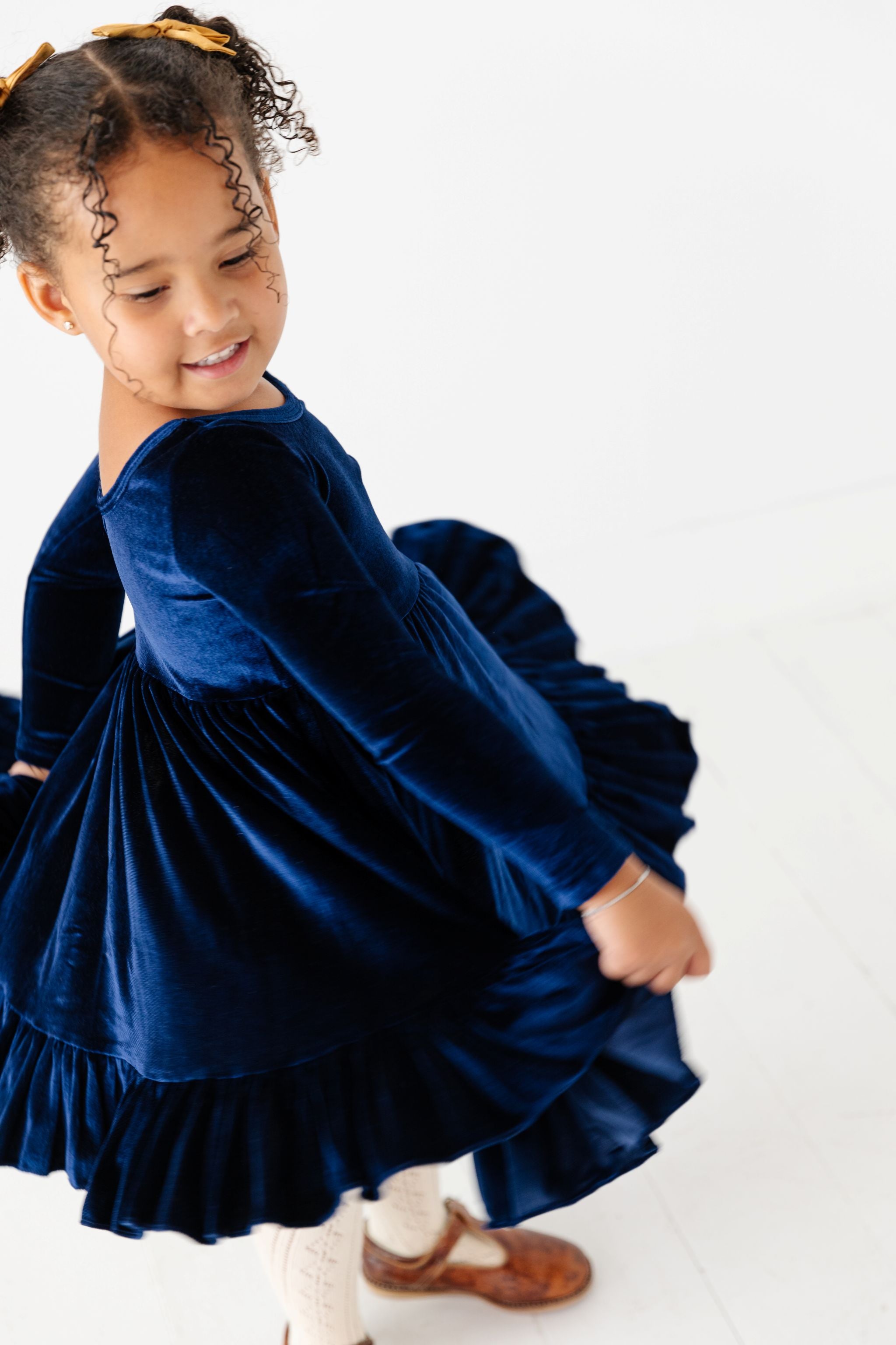 little girl twirling in navy blue long sleeve velvet twirl dress with cream open knit tights and gold satin pigtail bows