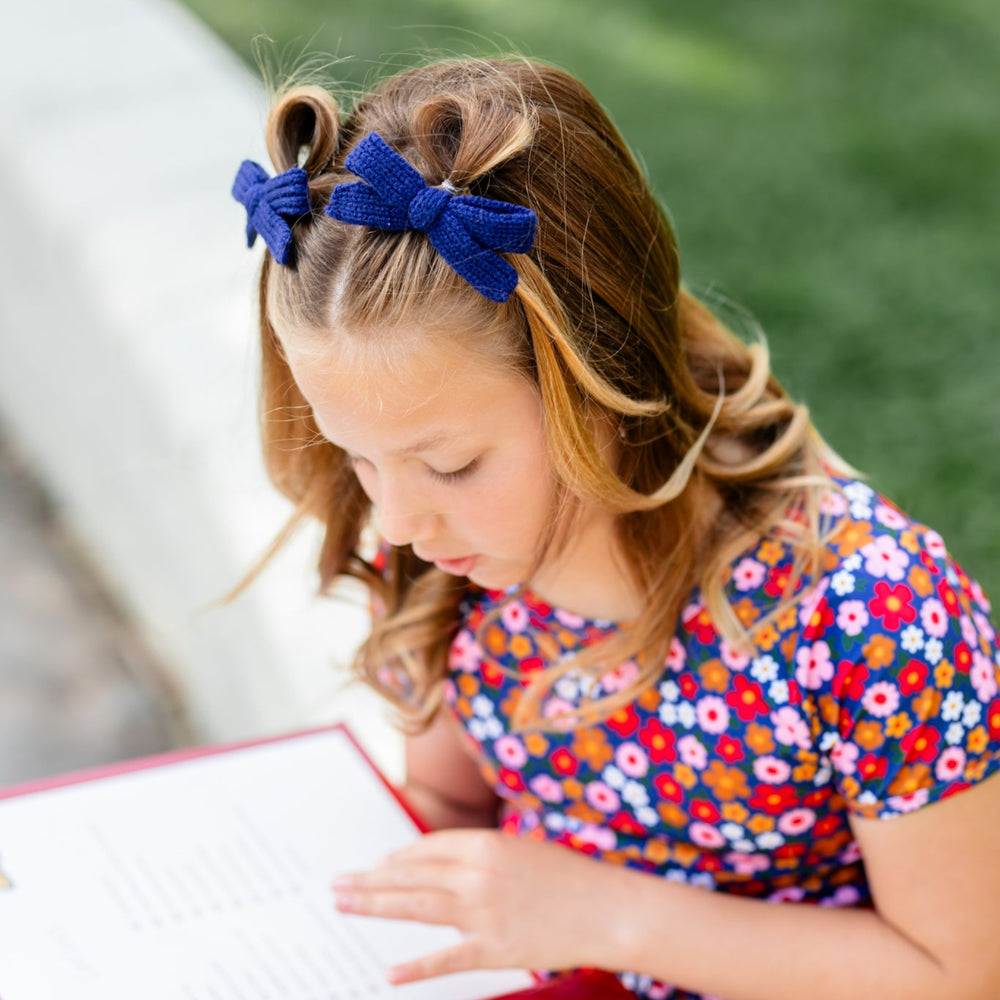 little girl reading book in navy blue knit pigtail bows and matching floral print set for school