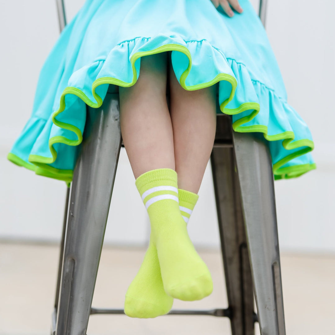 little girl sitting on stool in bright blue and neon green dress with matching neon striped midi socks