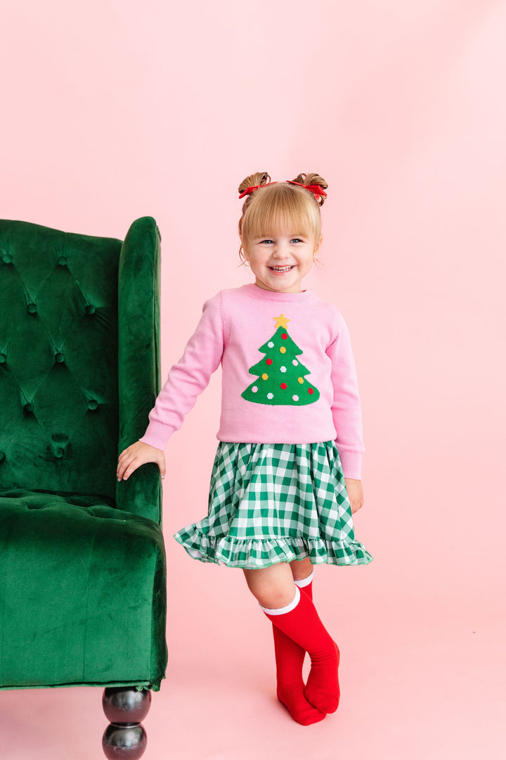 girl wearing pink christmas tree sweater with green gingham dress and knee high socks