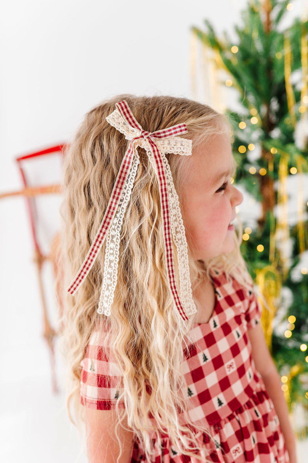 little girl with wavy blonde hair and vanilla lace and festive plad ribbon hair bow