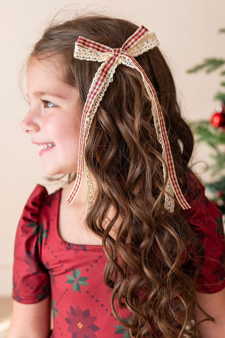 little girl with long curly wearing in poinsettia holiday dress and vanilla lace hair bow