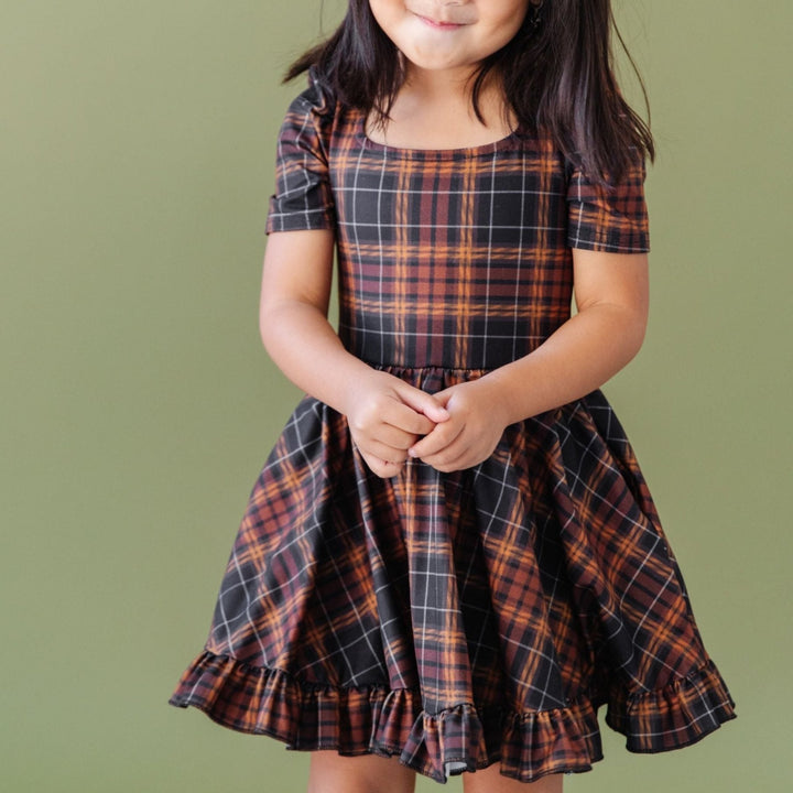 little girl in black and brown fall plaid twirl dress and matching mustard knee highs and pigtail bows