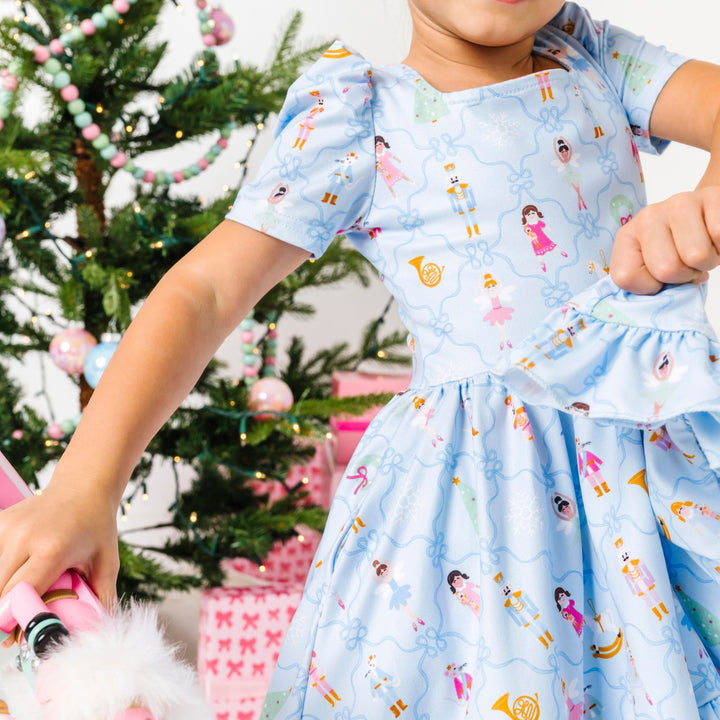 detail photo of girl dancing Iin light blue nutcracker print twirl dress in front of christmas tree