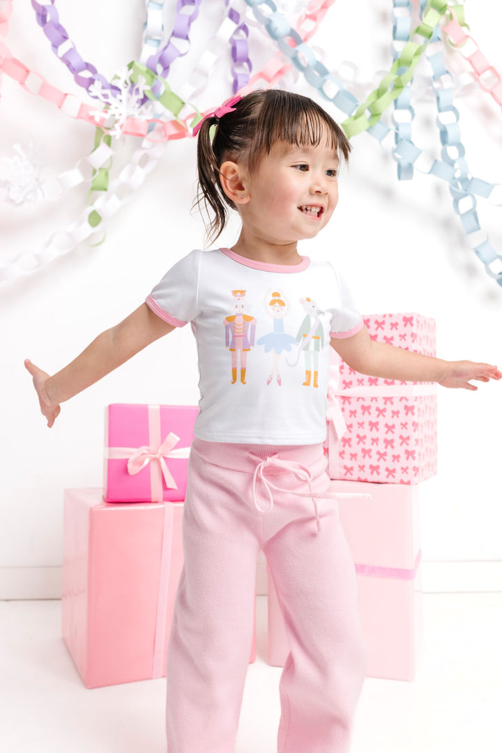 little girl dancing in front of pink Christmas gifts in Nutcracker inspired short sleeve top with pink binding and matching pink sweater pants