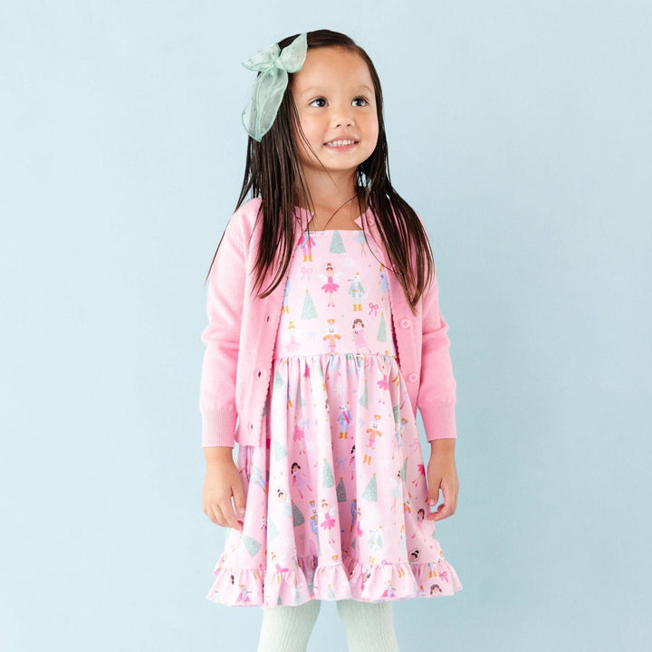 little girl wearing pink nutcracker print dress with matching mint tights and hair bow