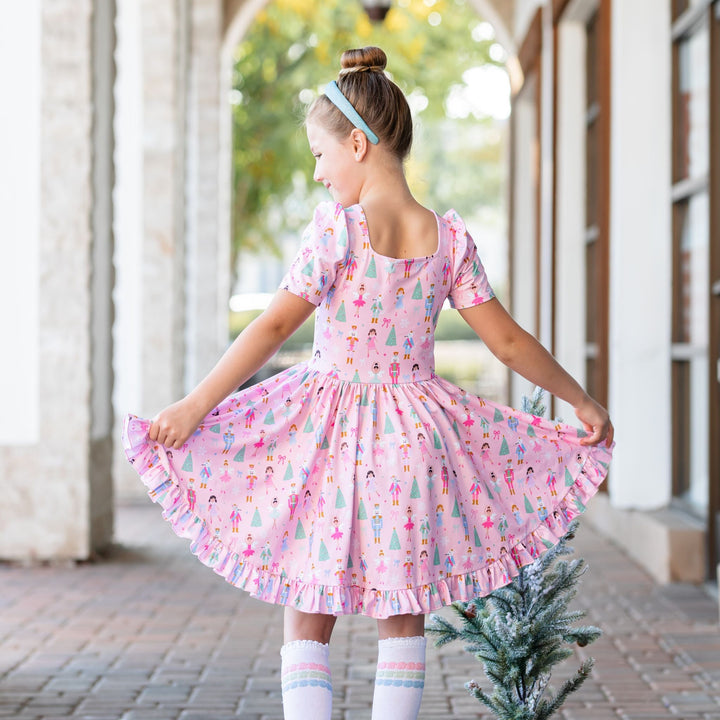 back view of little girl in pink nutcracker print square neck twirl dress for Chrismtas 