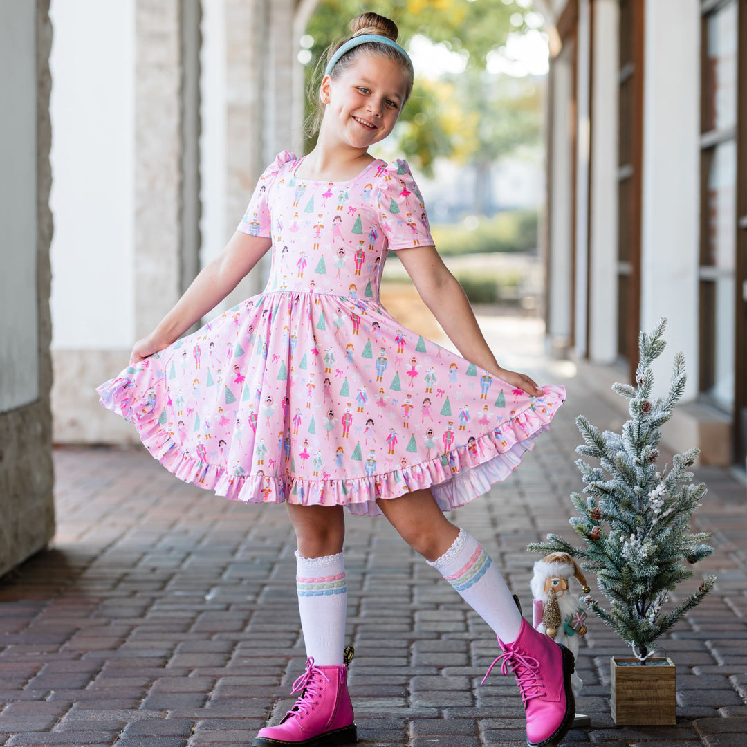 little girl in pink nutcracker themed twirl dress with matching blue sparkle headband and pastel knee highs for Christmas