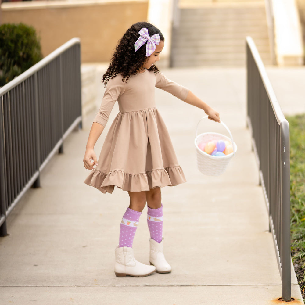little girl holding easter basket with tan neutral twirl dress and purple easter bunny knee hgih socks
