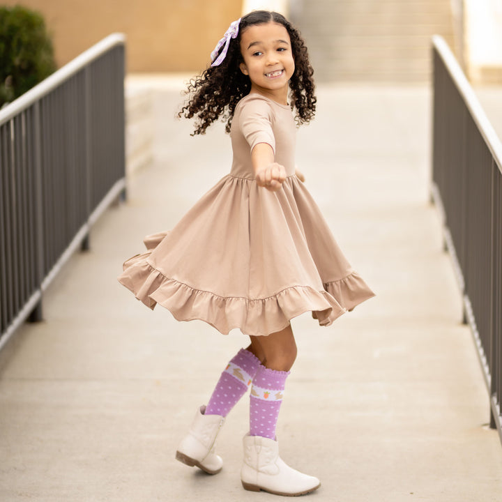 little girl twirling in neutral oat twirl dress with pockets and cute purple easter bunny socks