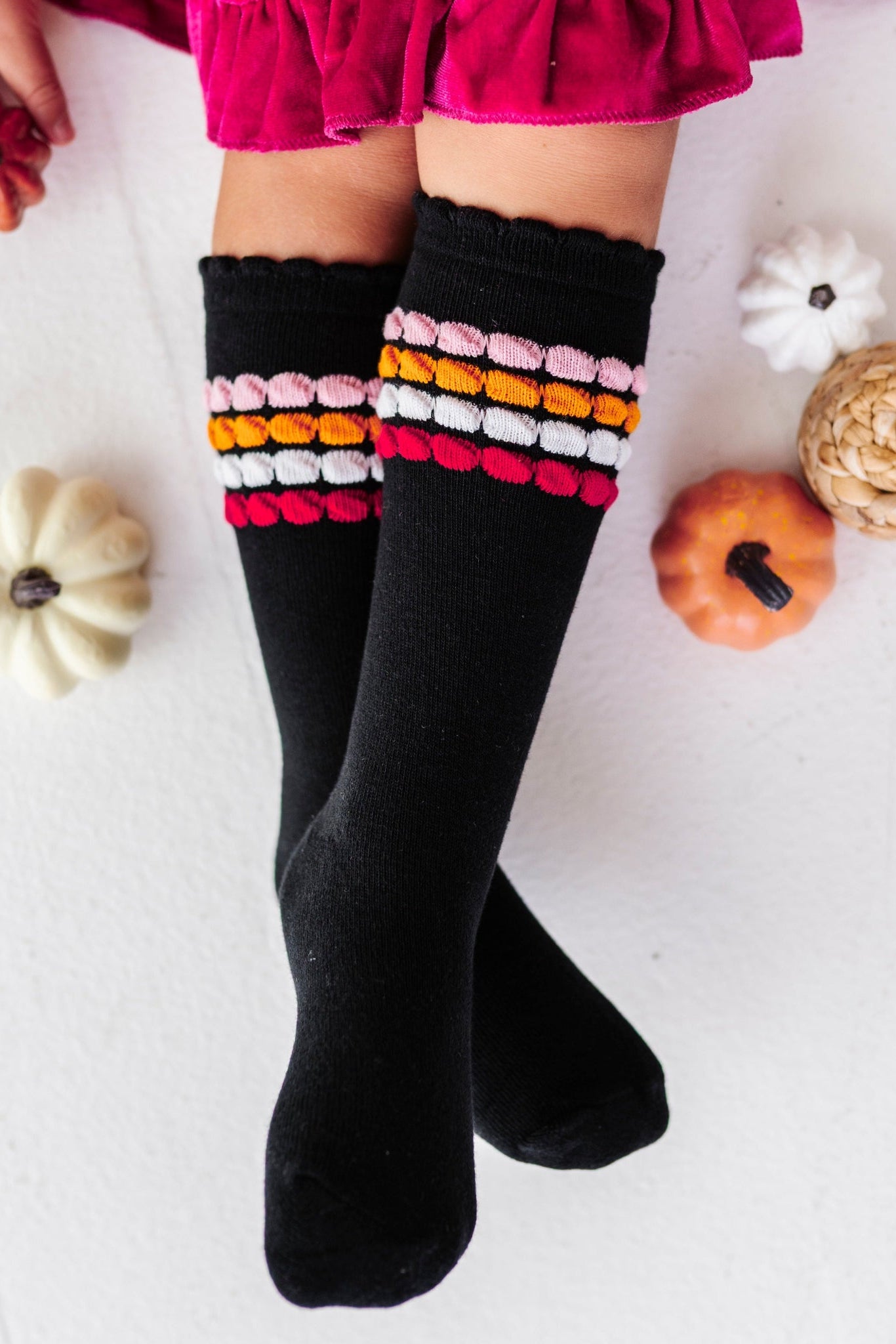 young girl holding pumpkin decor in hot pink velvet twirl dress paired with black knee socks with pink and orange bubble stripes at the calf and lace trim