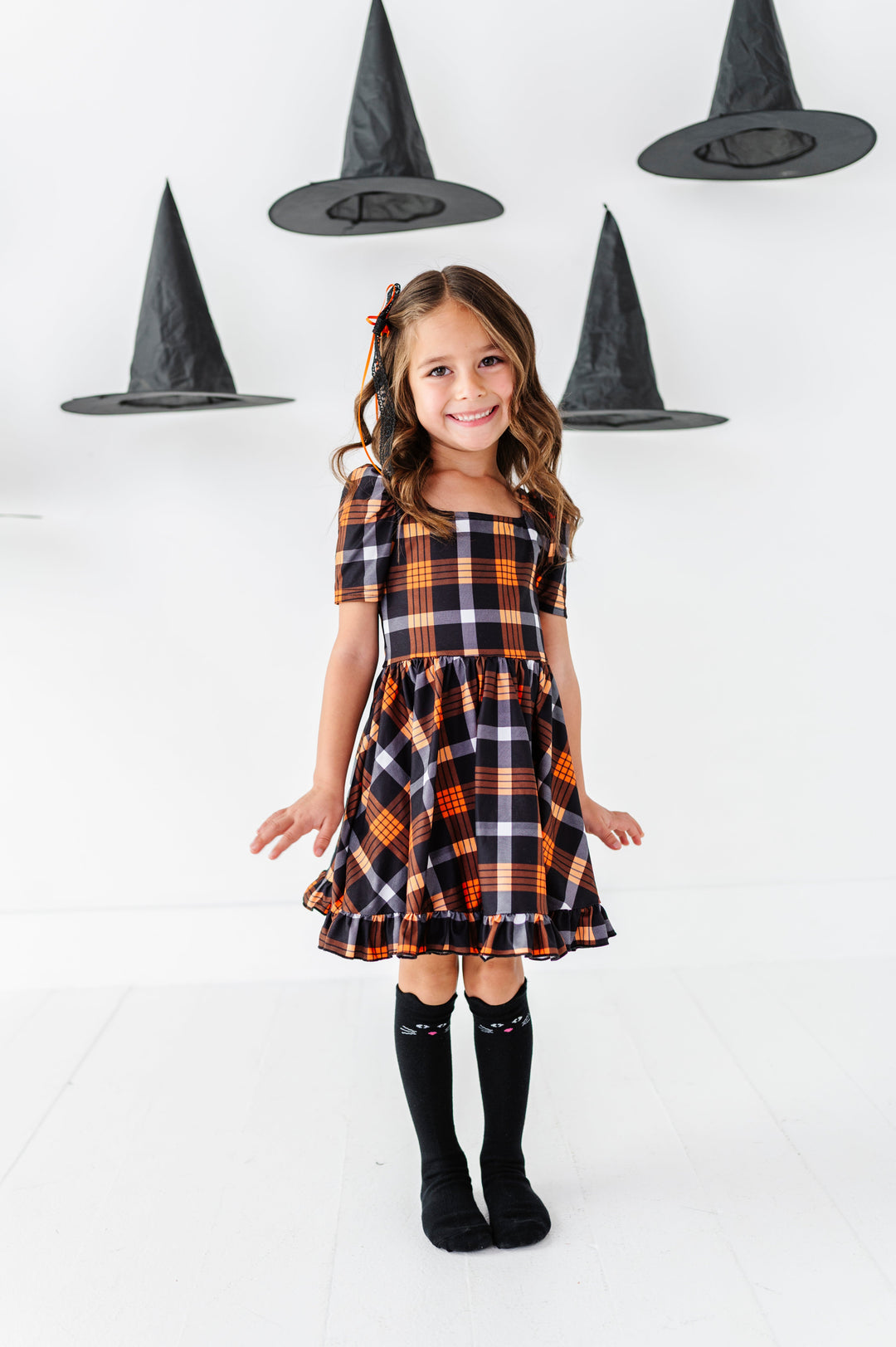 young girl surrounded by floating witch hats in black and orange plaid square neck twirl dress paired with black cat knee socks