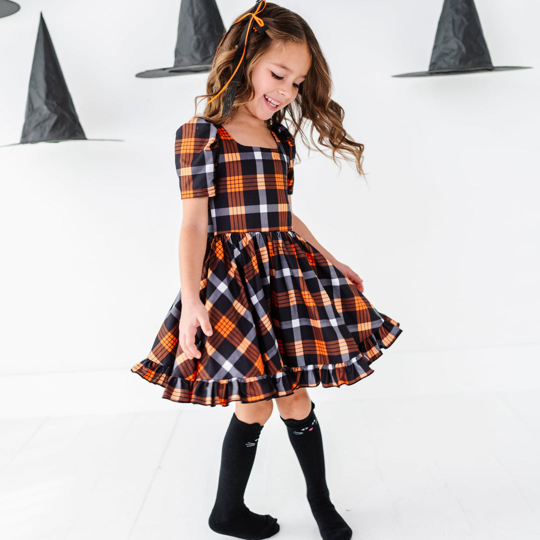 young girl twirling with witch hats overhead in black and orange short sleeve twirl dress paired with black cat design knee socks and black and orange lace ribbon hair bow