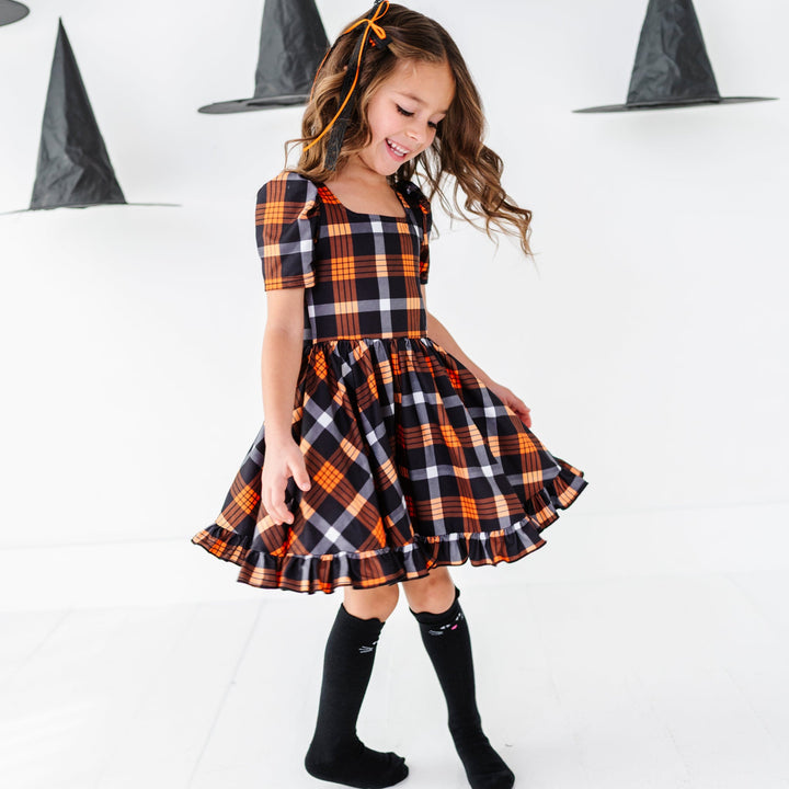 young girl twirling with witch hats overhead in black and orange short sleeve twirl dress paired with black cat design knee socks and black and orange lace ribbon hair bow
