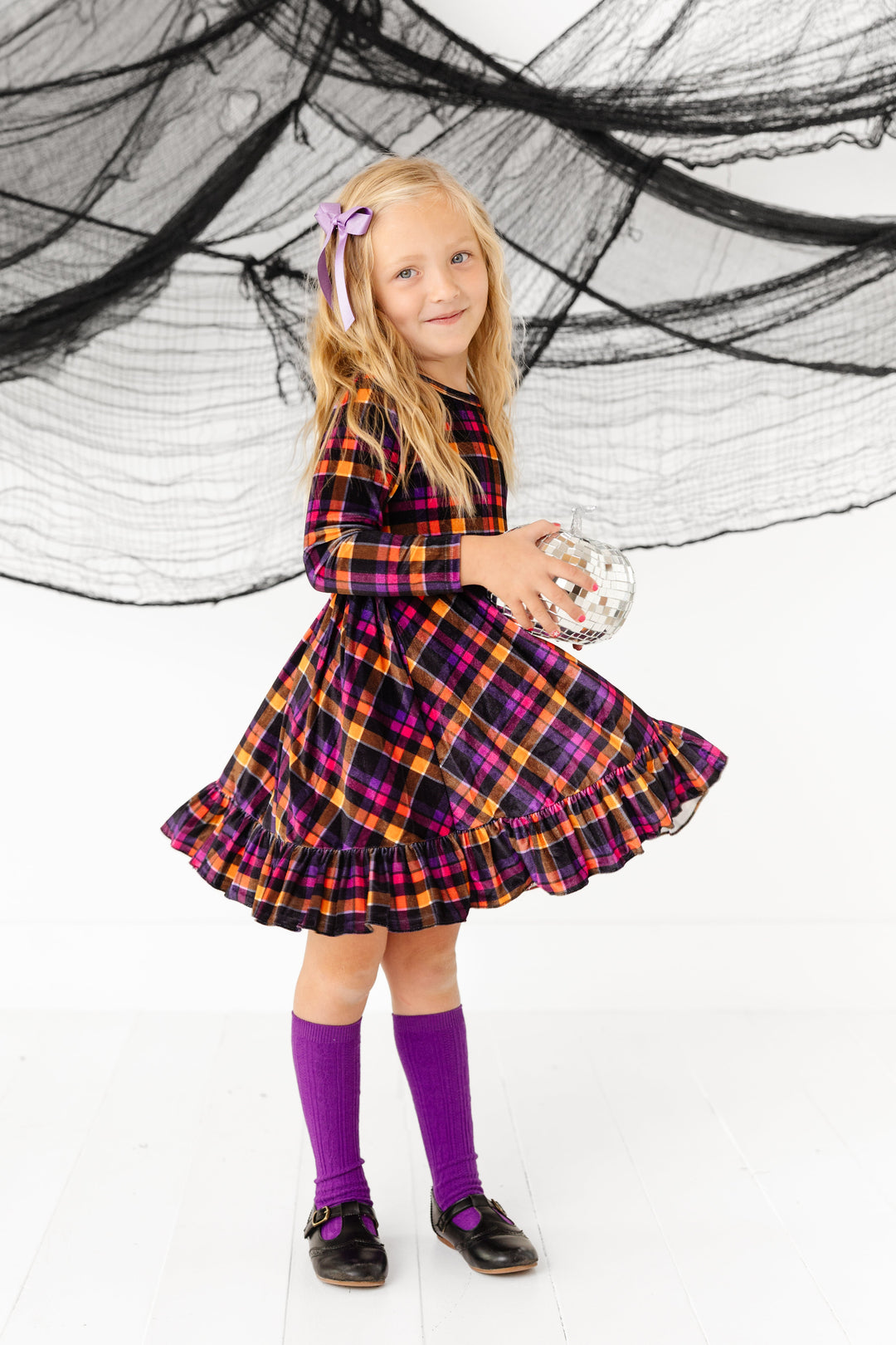 little girl twirling in long sleeve velvet plaid dress in Halloween colors with matching purple knee highs and lavender shimmery ribbon hairbow