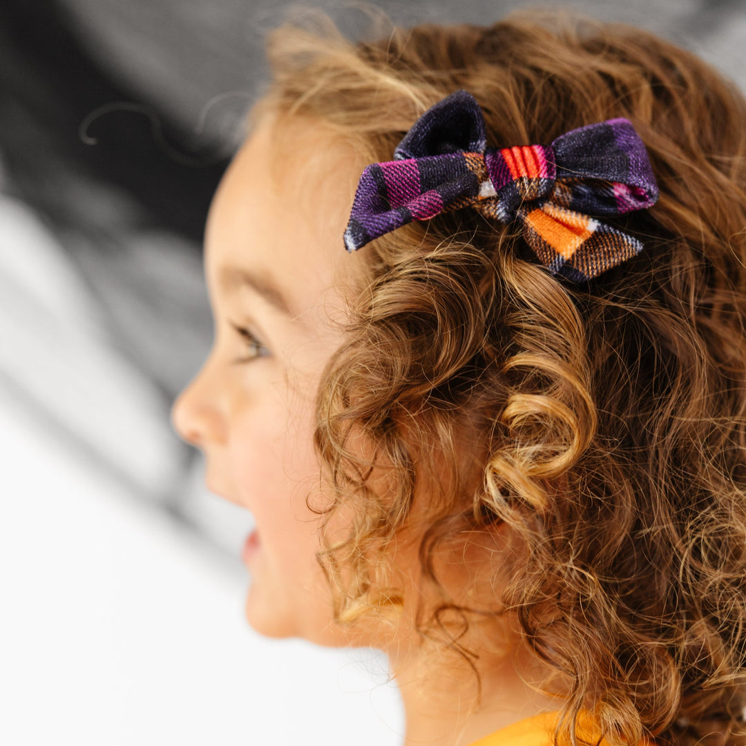 little girl in orange Halloween top with matching Halloween plaid velvet bow on clip