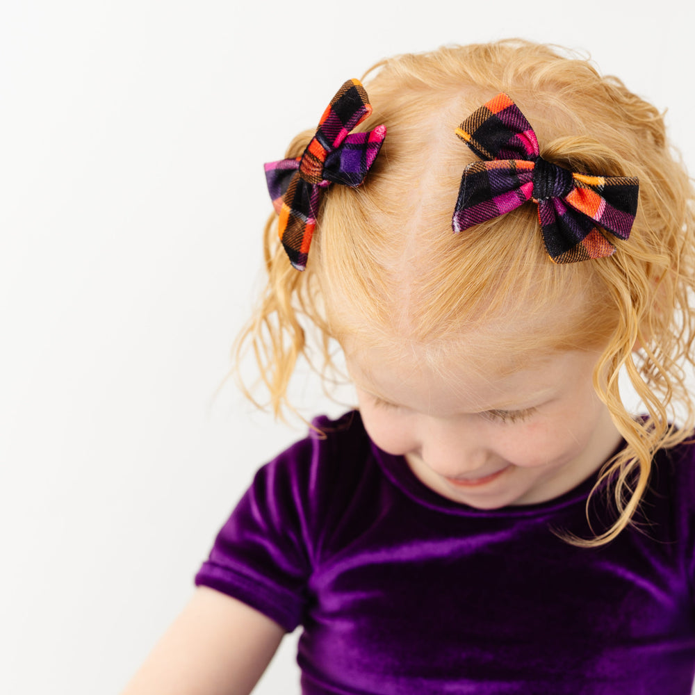 little girl in Halloween purple velvet top and matching plaid velvet pigtail bows on clips