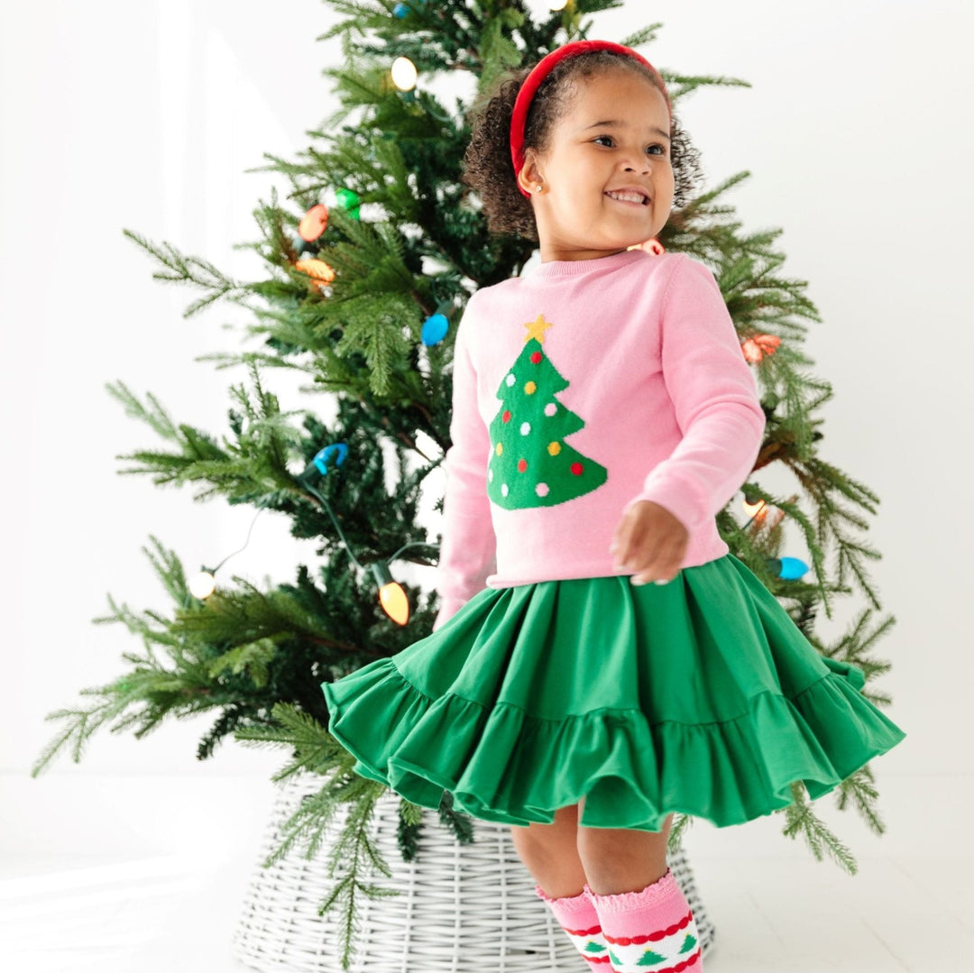 little girl twirling in pink sweater with Christmas tree and matching green dress