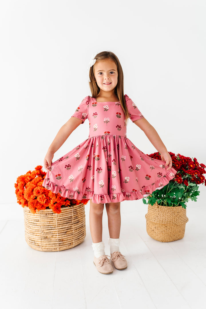 little girl standing in front of fall floral baskets in rosy pink twirl dress with ivory and rust flower print paired with ivory lace bobby socks and hair bow