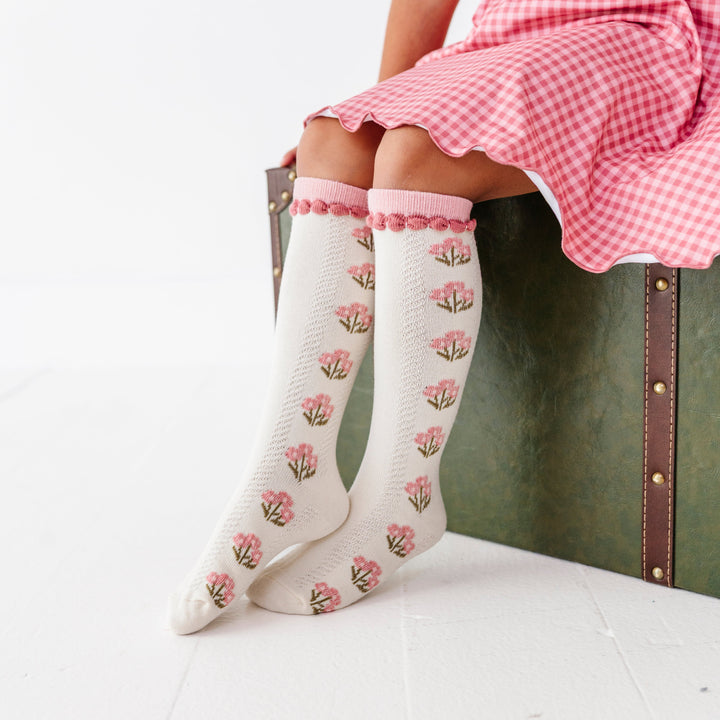 little girl sitting on vintage suitcase wearing ivory knee socks with fall pink floral design and matching trim paired with old rose gingham twirl dress