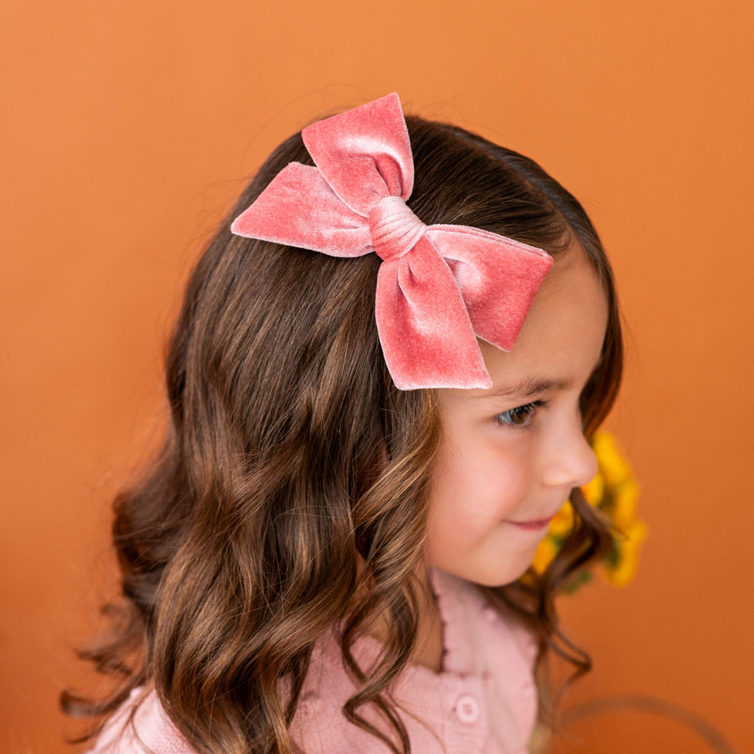 young girl in front of orange backdrop in pink velvet hair bow paired with light pink fall cardigan