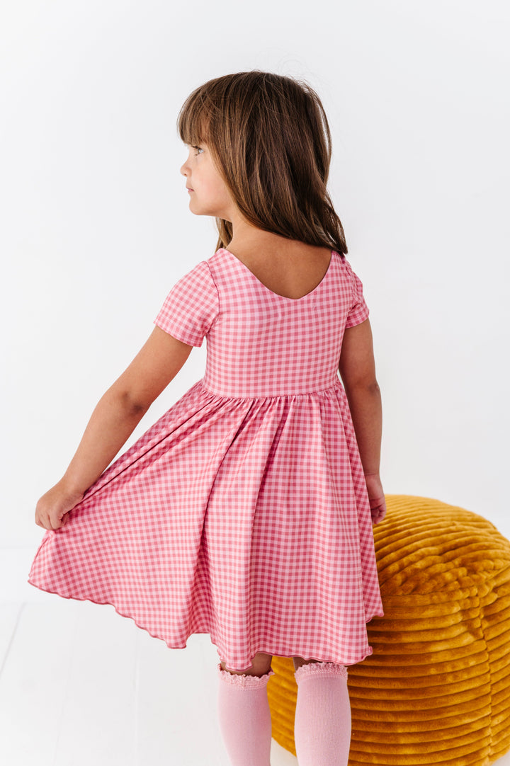back detail photo of little girl in v-neck short sleeve pink gingham twirl dress paired with pink knee socks