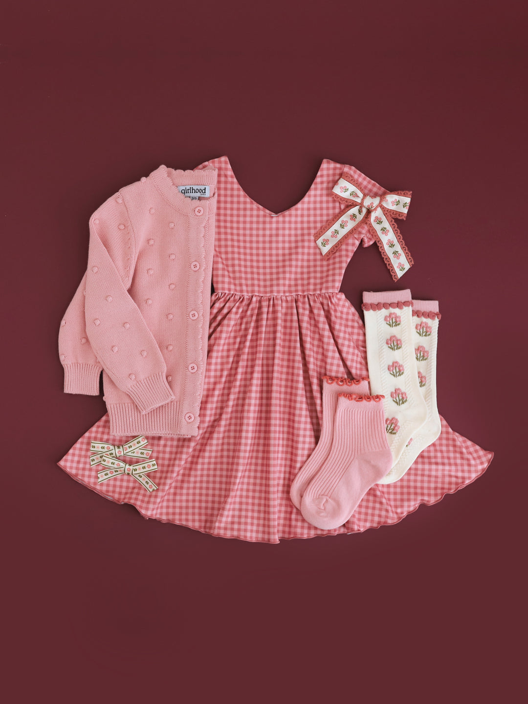 styled flat lay photo of girls' pink gingham twirl dress paired with matching pink sweater and accessories for fall