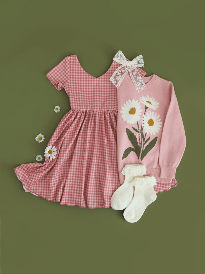 flat lay of pink gingham twirl dress with v-neck paired with matching pink floral sweater and cream lace bobby socks and bow