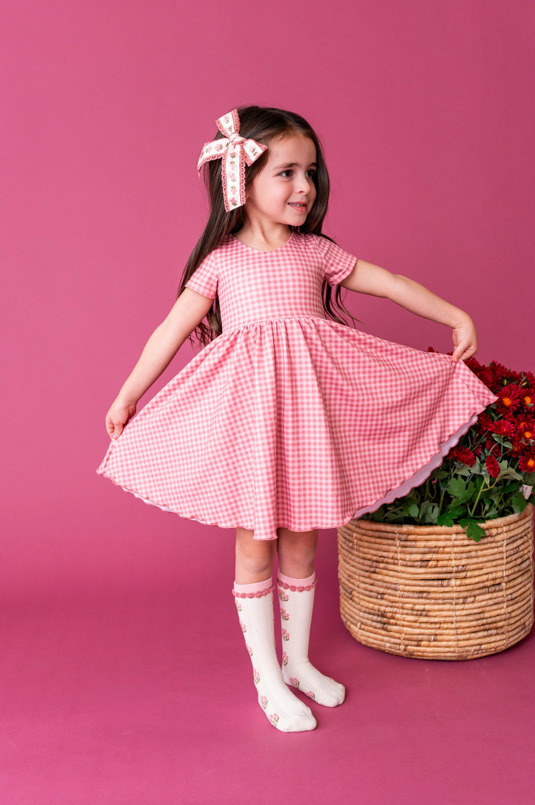 little girl in pink gingham twirl dress paired with matching floral knee socks and floral bow with lace trim