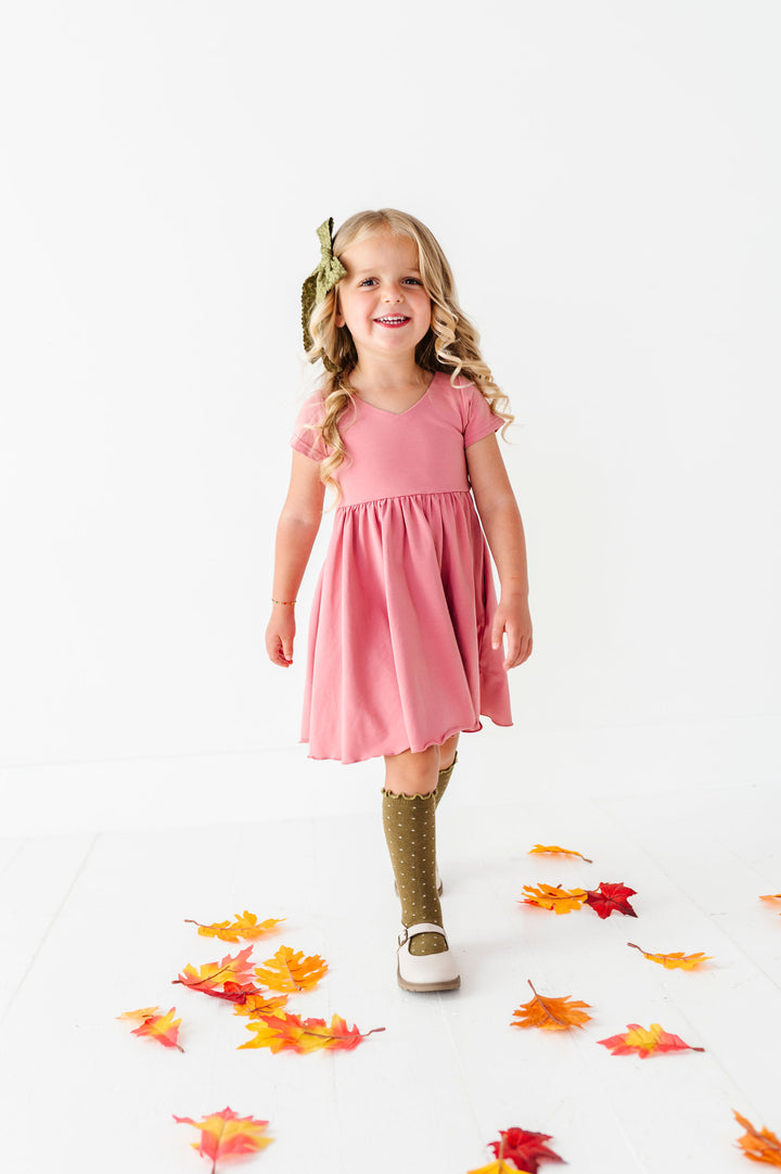 little girl walking in fall leaves wearing rose pink dress with olive green knee high socks