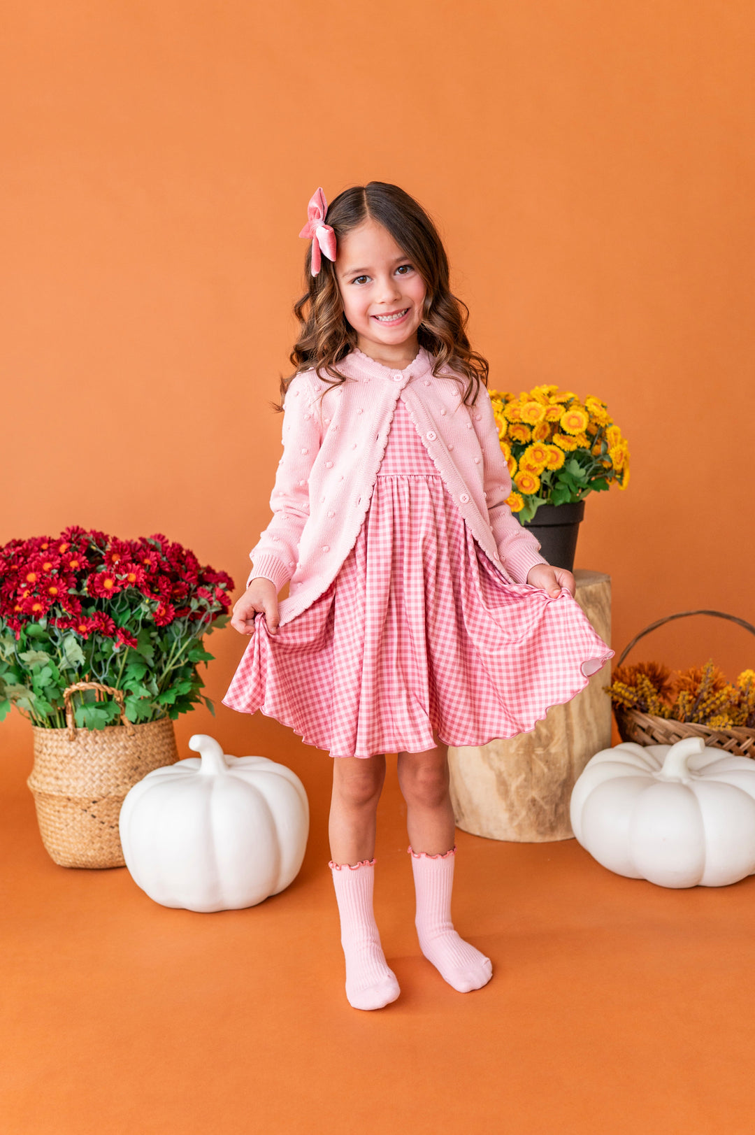 young girl in front of fall pumpkins and florals in pink gingham twirl dress and matching light pink accessories