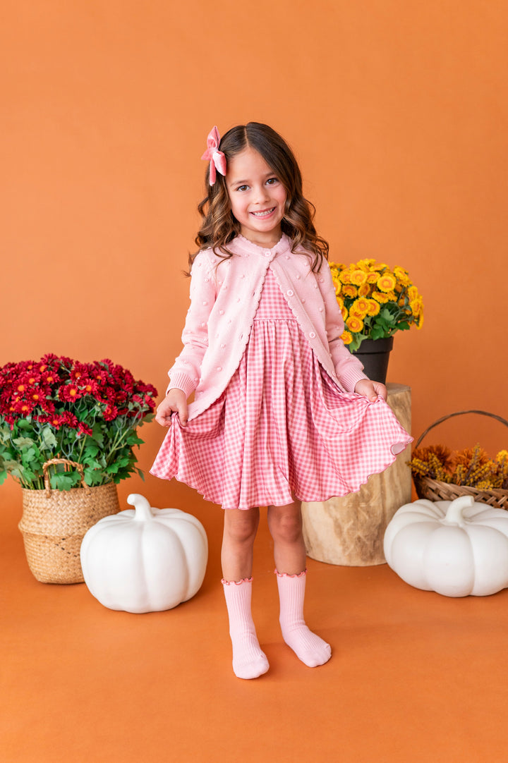 young girl in front of fall pumpkins and florals in pink gingham twirl dress and matching light pink accessories