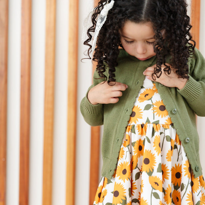 little girl in sunflower print twirl dress and matching olive green button front knit cardigan