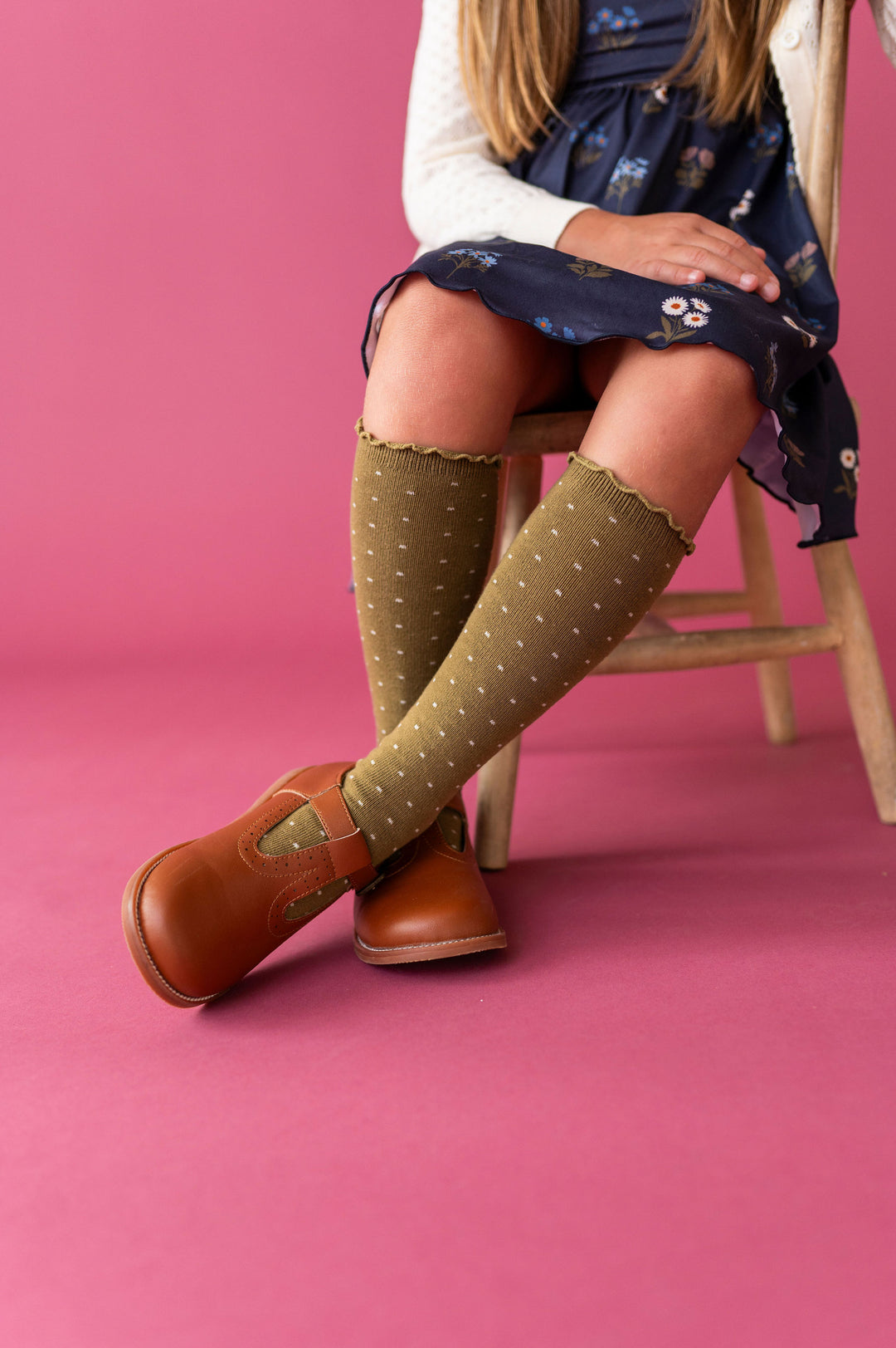 girl sitting down wearing olive green dotted knee high socks with fall shoes