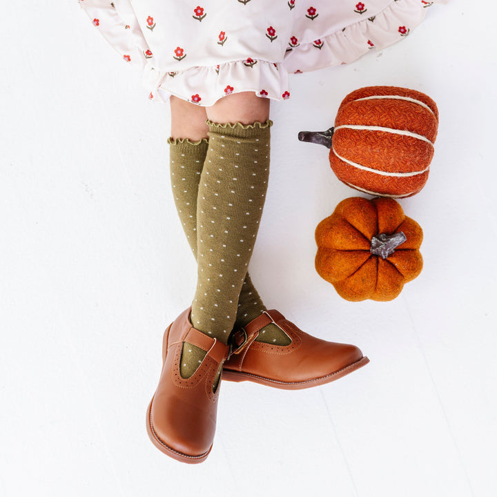 girl sitting by felt pumpkins in olive green with ivory dot knee socks paired with cream floral fall dress