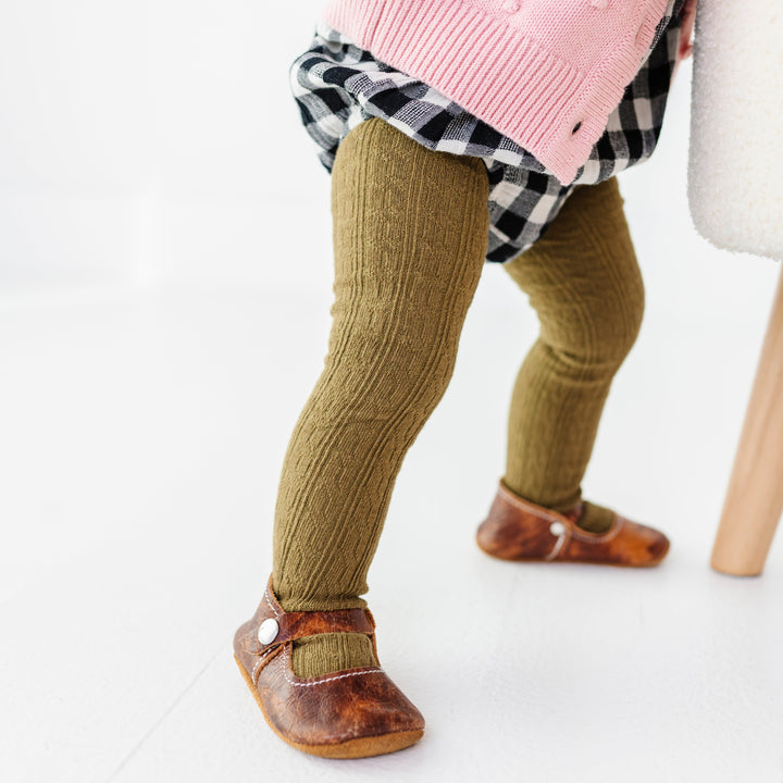 baby girl in olive cable knit tights paired with soft soled mary jane shoes and buffalo plaid romper for fall