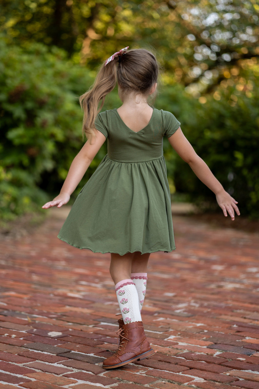 young girl twirling in olive v-neck twirl dress paired with pink floral knee socks