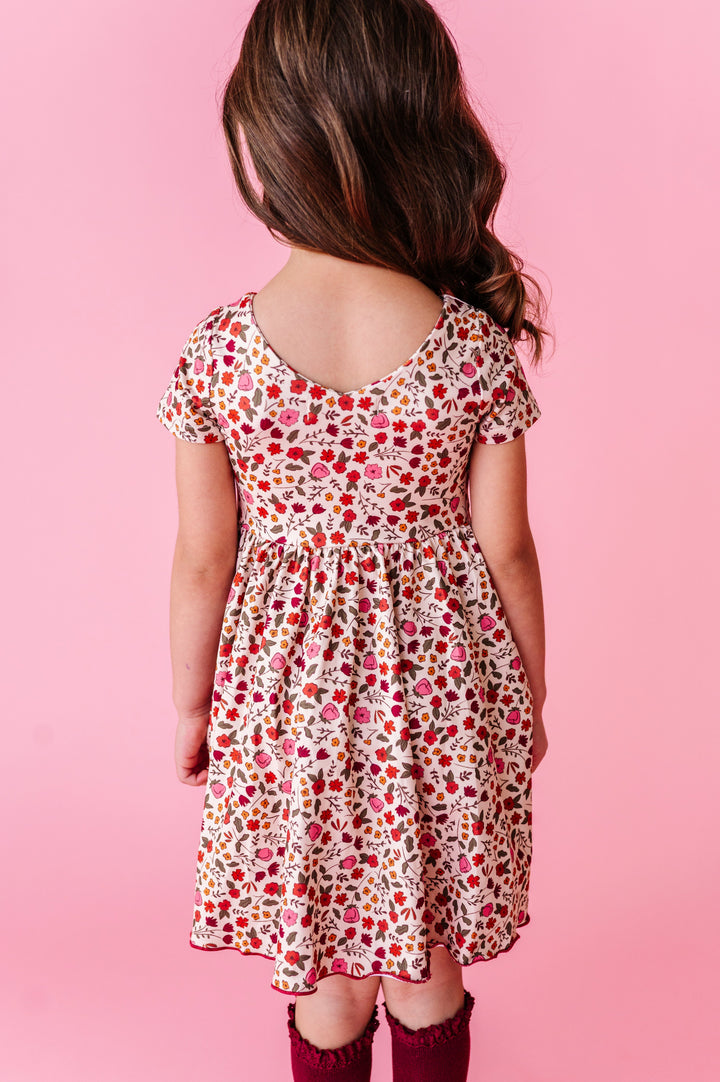 young girl standing against pink backdrop in cream v-neck twirl dress with fall floral pattern