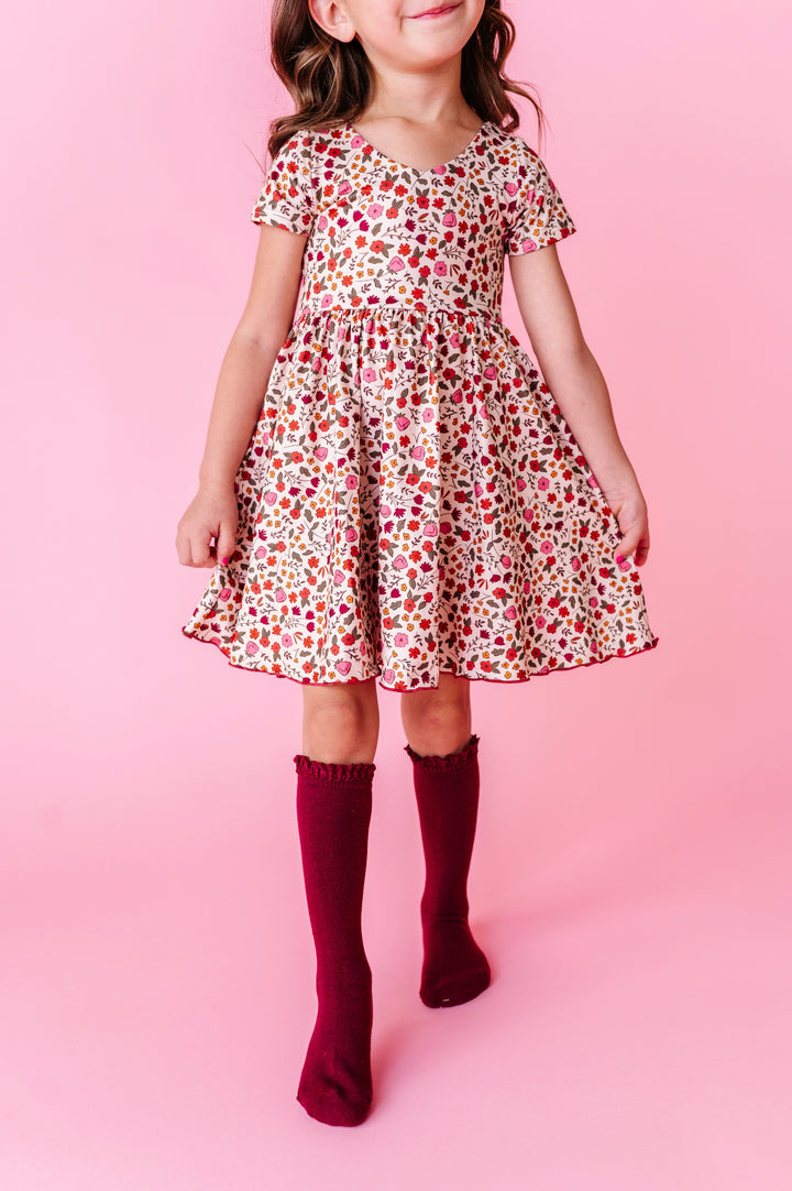 young girl in front of pink backdrop in fall floral dress paired with matching burgundy lace top knee socks