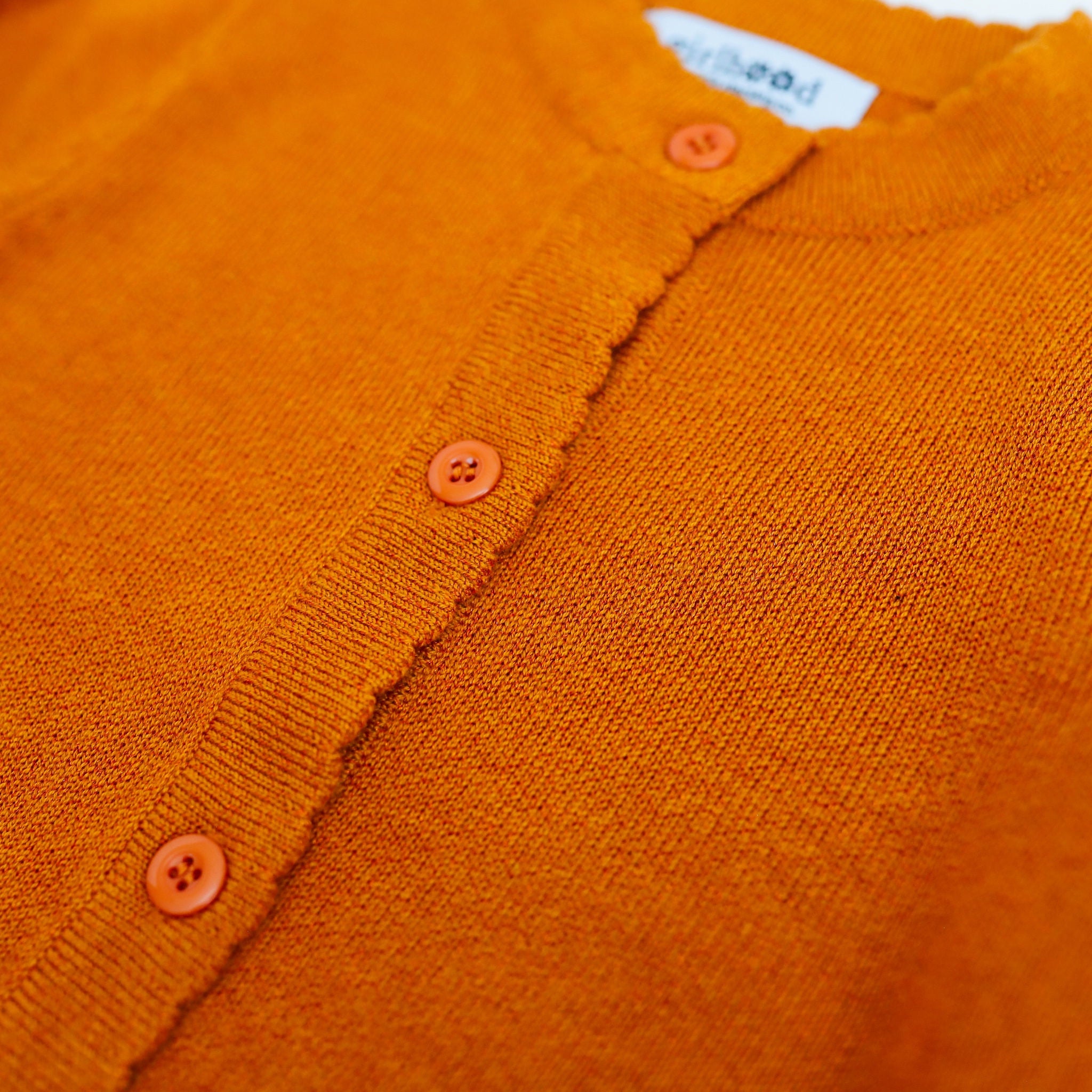 detail of scalloped placket and subtle sparkle orange sweater