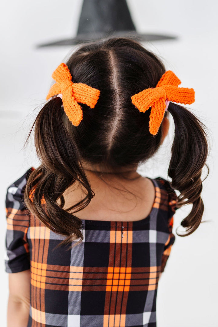 little girl in halloween plaid dress and orange yarn pigtail hair bows