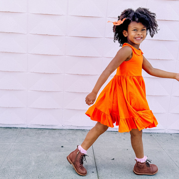 little girl walking outside in bright orange summer cotton twirl dress with pockets and peter pan collar