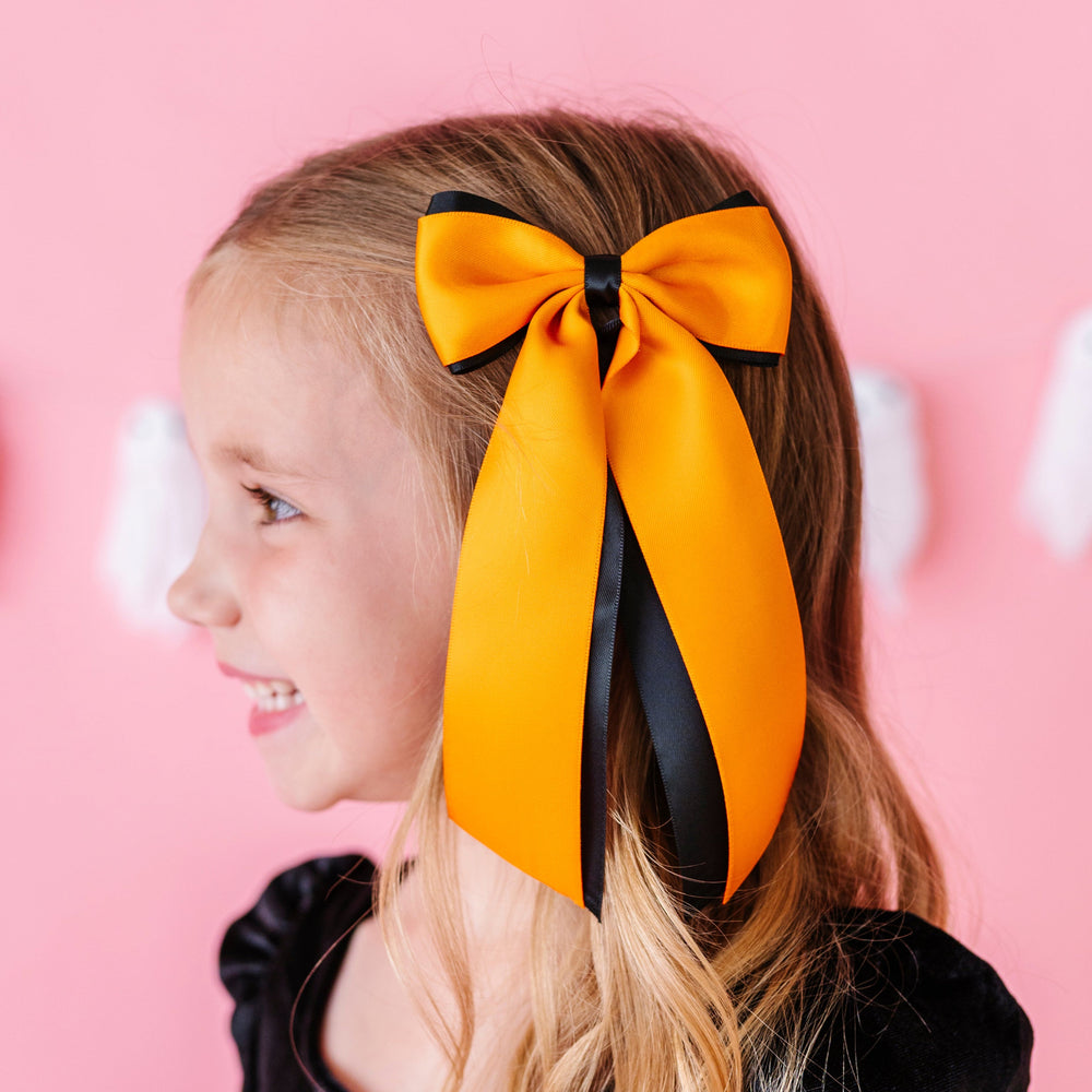 little girl in wide orange and black layered ribbon bow on clip for Halloween paired with black velvet dress
