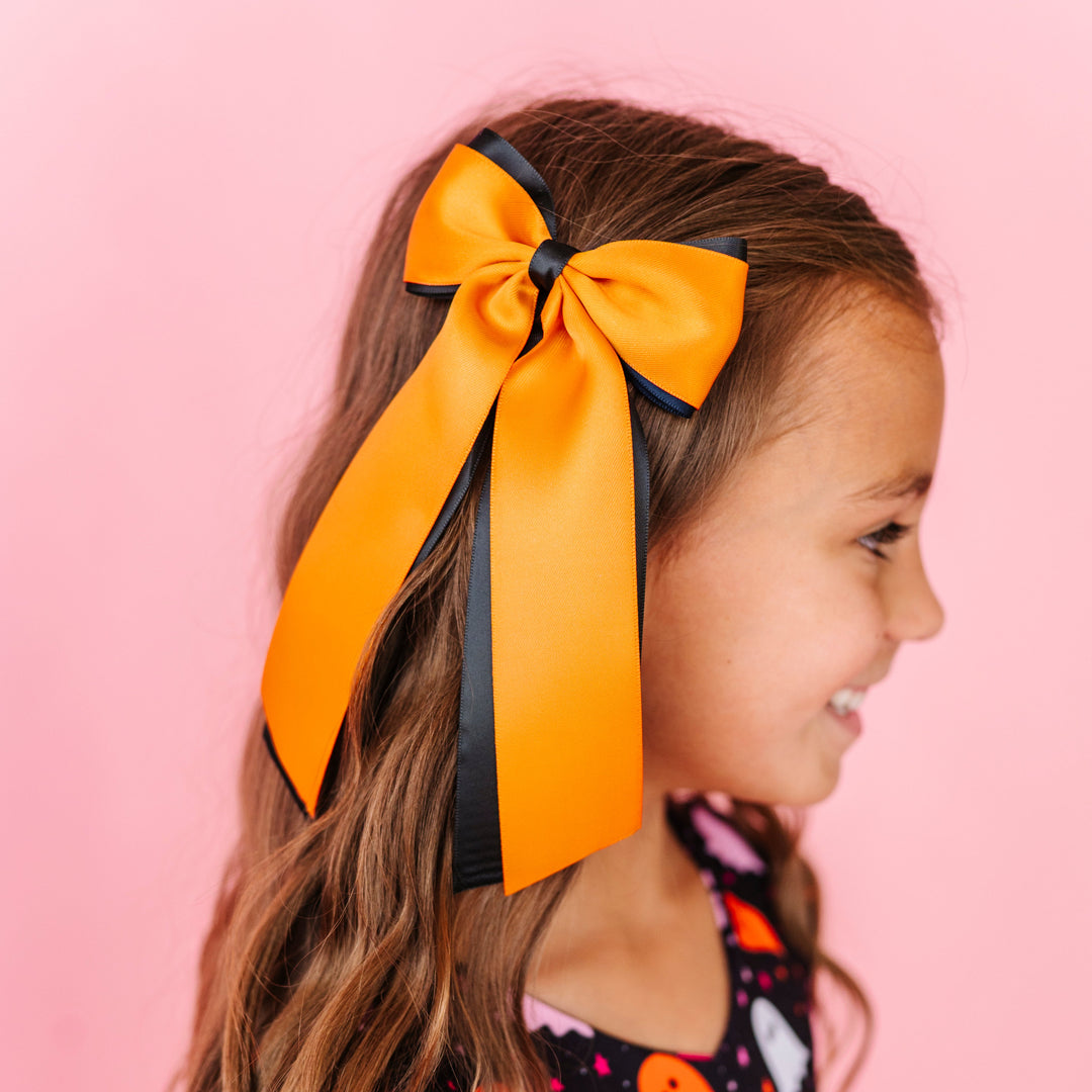 young girl in ghost print twirl dress paired with wide black and orange layred ribbon hair bow