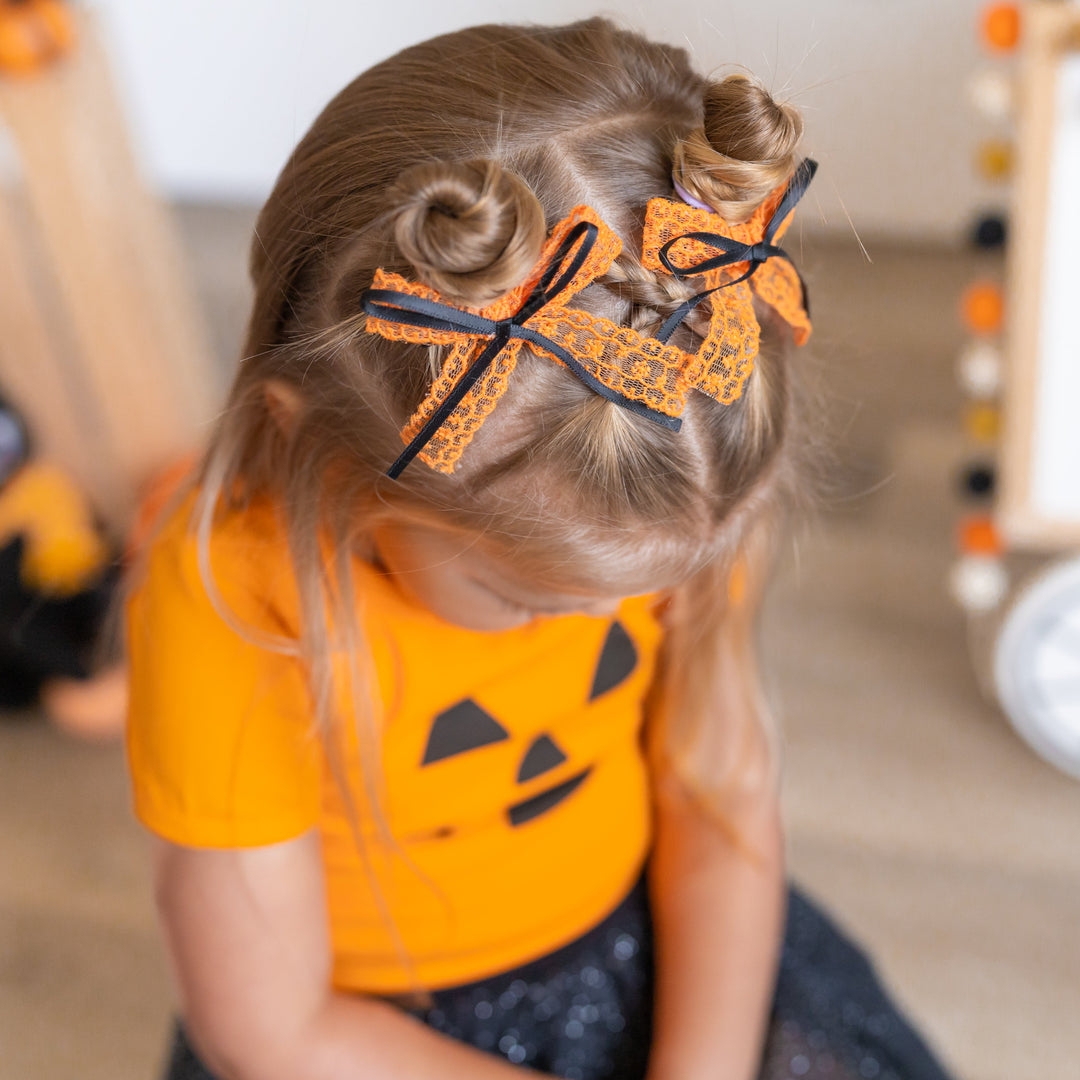 little girl in orange jack-o-lantern top paired with orange lace with black ribbon pigtail bows on clips