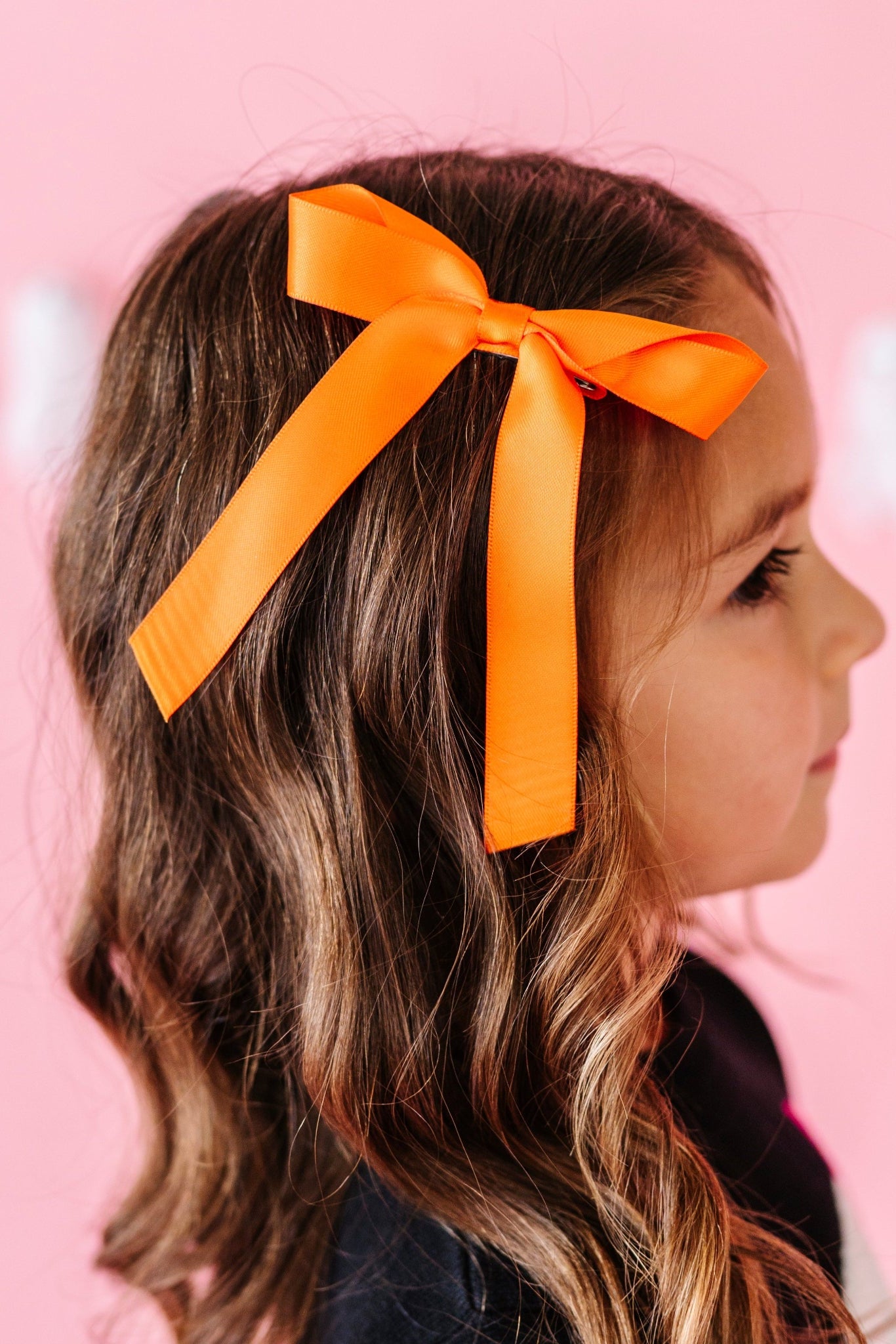young girl in front of ghost garland in bright Halloween orange ribbon hair bow on clip and black ghost sweater