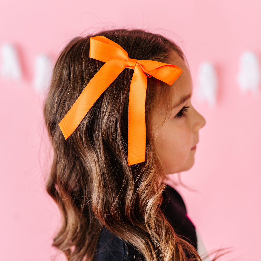 young girl in front of ghost garland in bright Halloween orange ribbon hair bow on clip and black ghost sweater