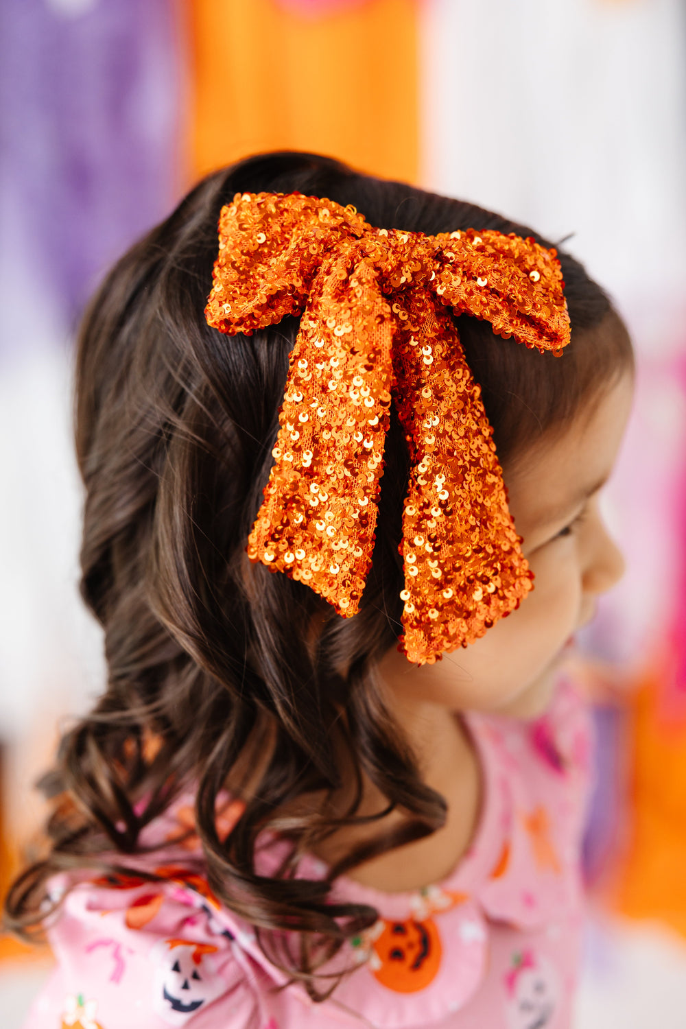 closeup of little girl in Halloween orange bow with sequins paired with pink pumpkin print twirl dress
